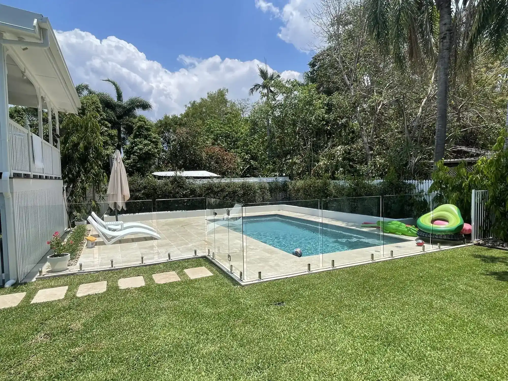 Frameless glass pool fence around a home pool beside a Queenslander-style house