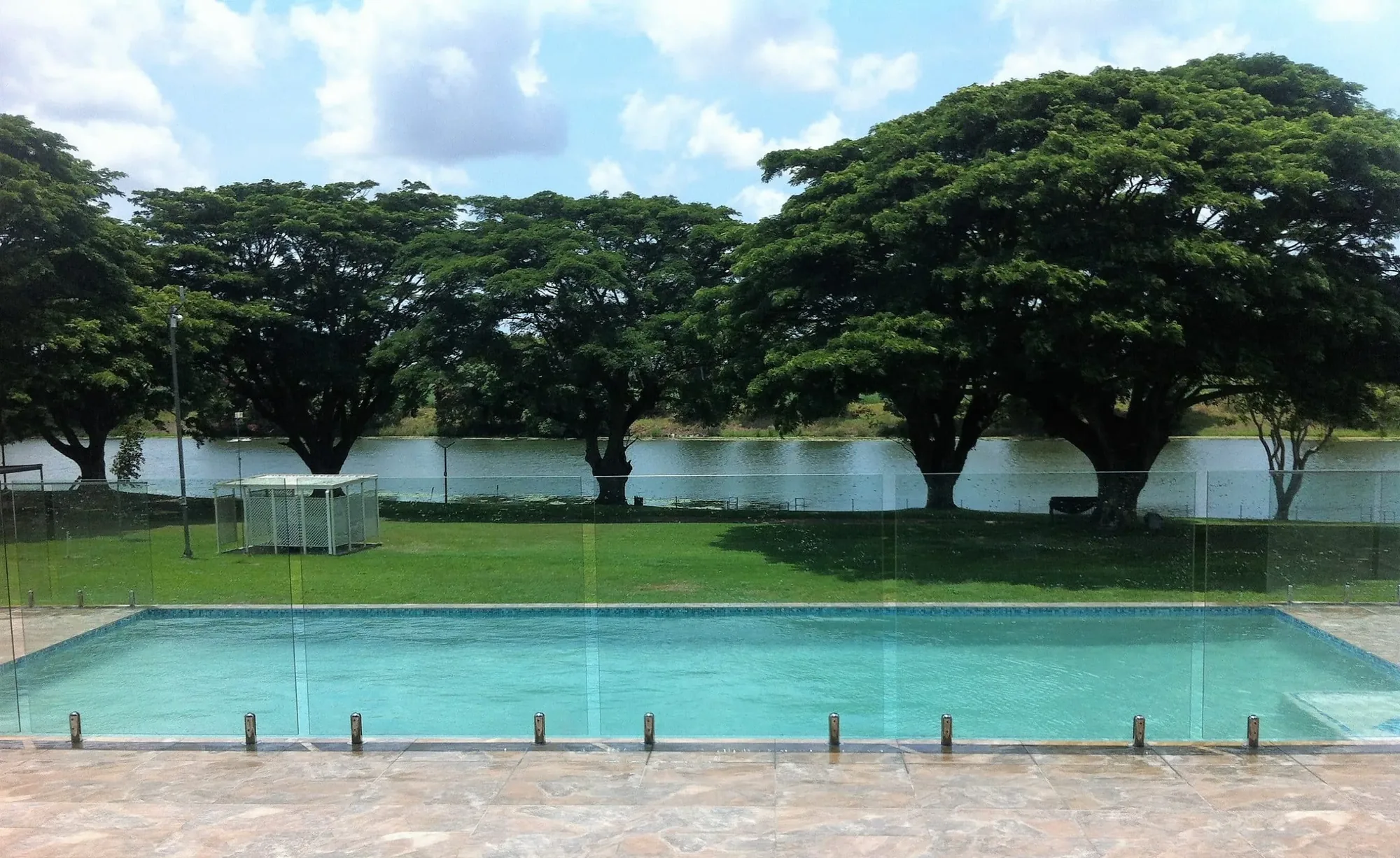 Glass pool fence beside a lakeside pool surrounded by shade trees