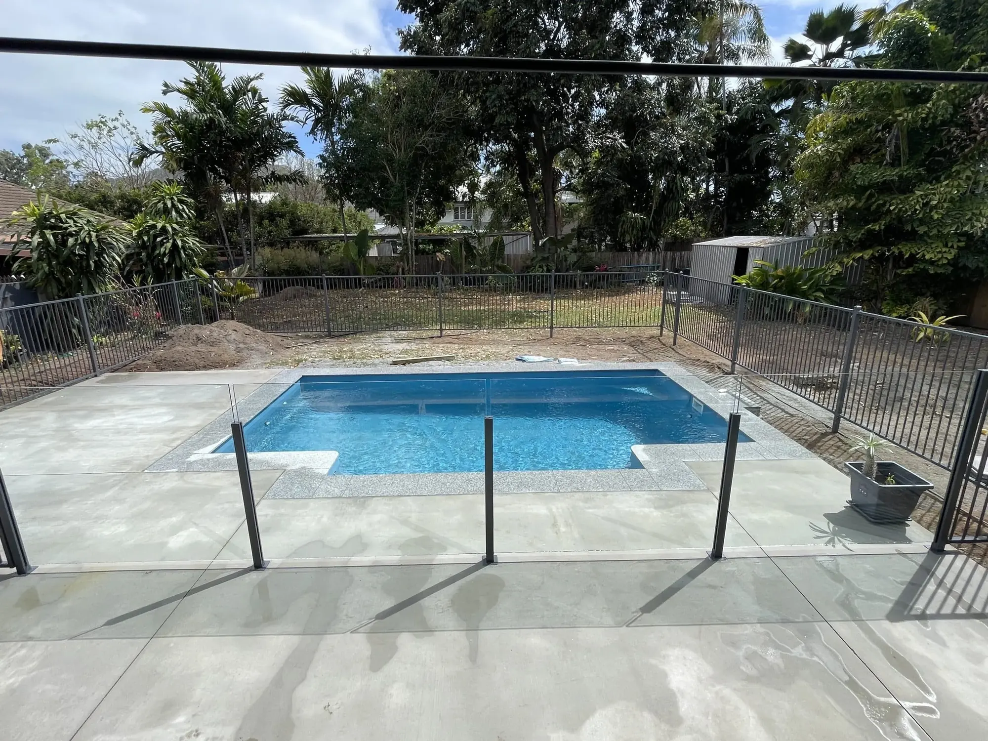 Black metal pool fence and glass panel combination around a newly built pool
