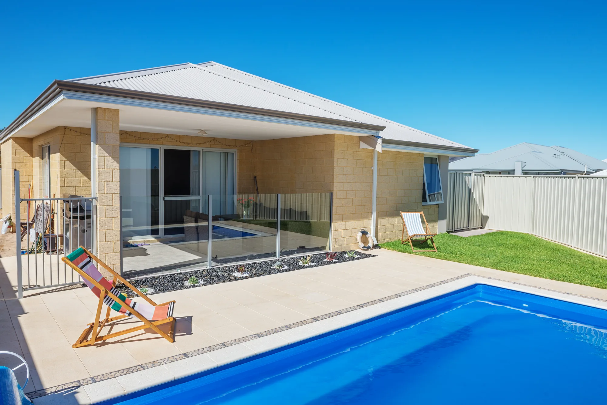 Glass pool fence around a sandstone-brick home pool