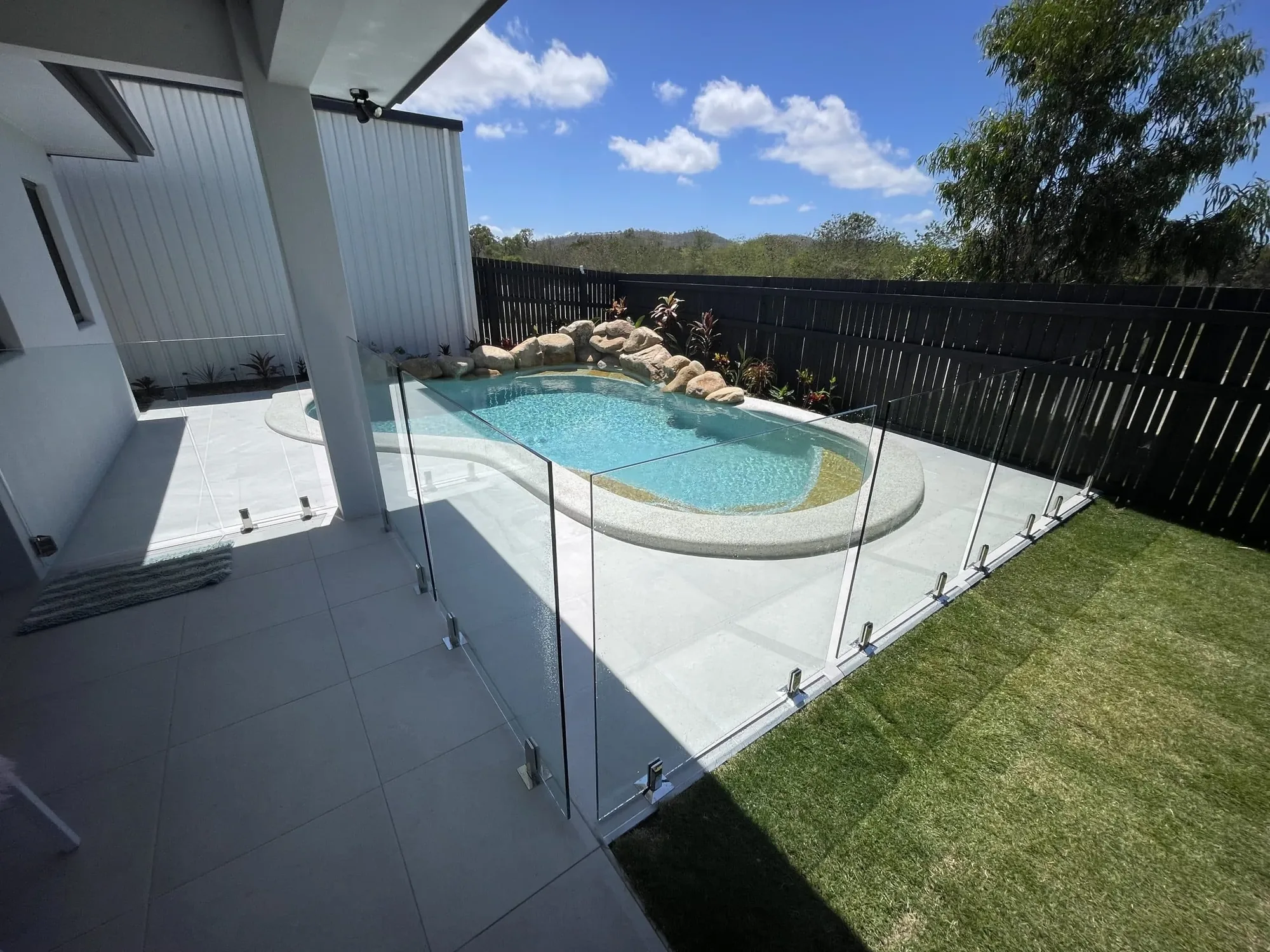 Glass pool fence around a freeform pool with a natural rock feature