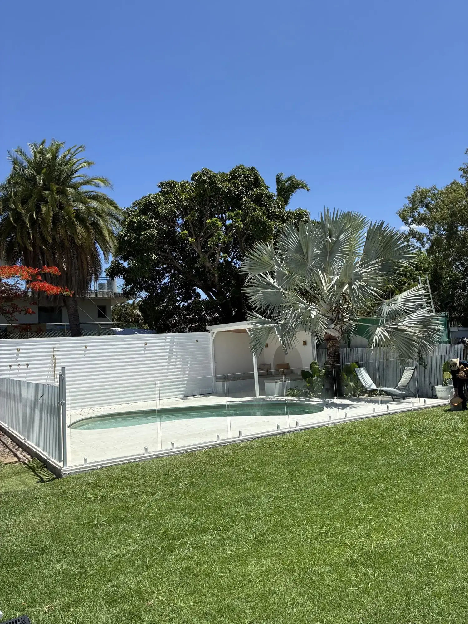 Glass pool fence around a kidney-shaped pool in a tropical garden